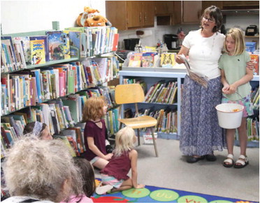 TAMMI FLADAGER, standing left, reads ….